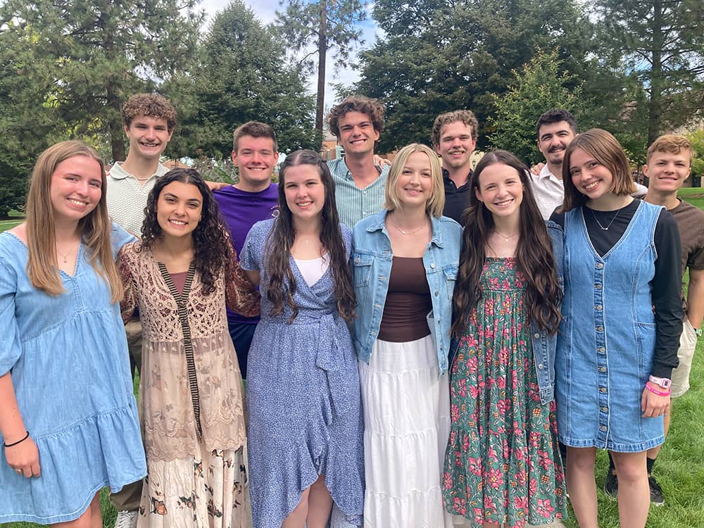 12 students pose for a photo on a grassy lawn with trees in the background.