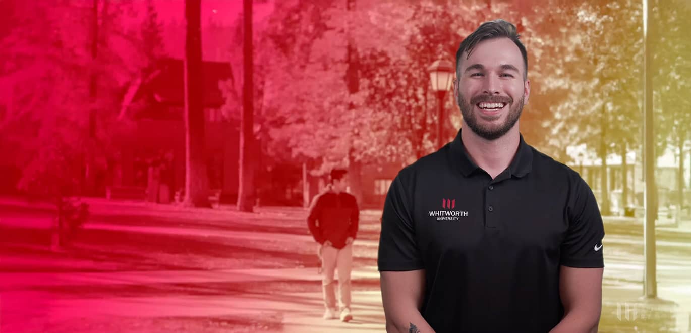 A Whitworth staff members stands, smiling, in front of a blurred and red-tinted backdrop.