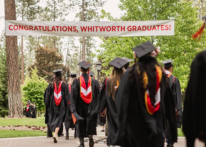 A group of Whitworth graduates walk away from the camera, wearing graduation regalia.