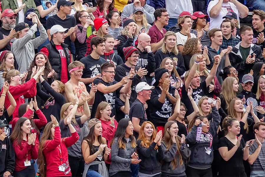A crowd of students fills an outdoor stadium, wearing Whitworth colors and celebrating.