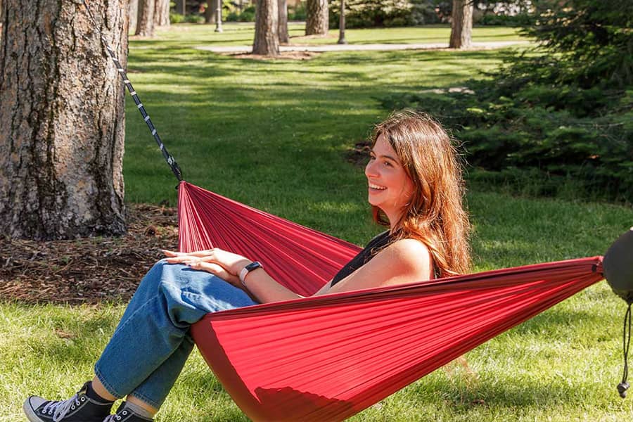 A student enjoys a sunny break in a red hammock.
