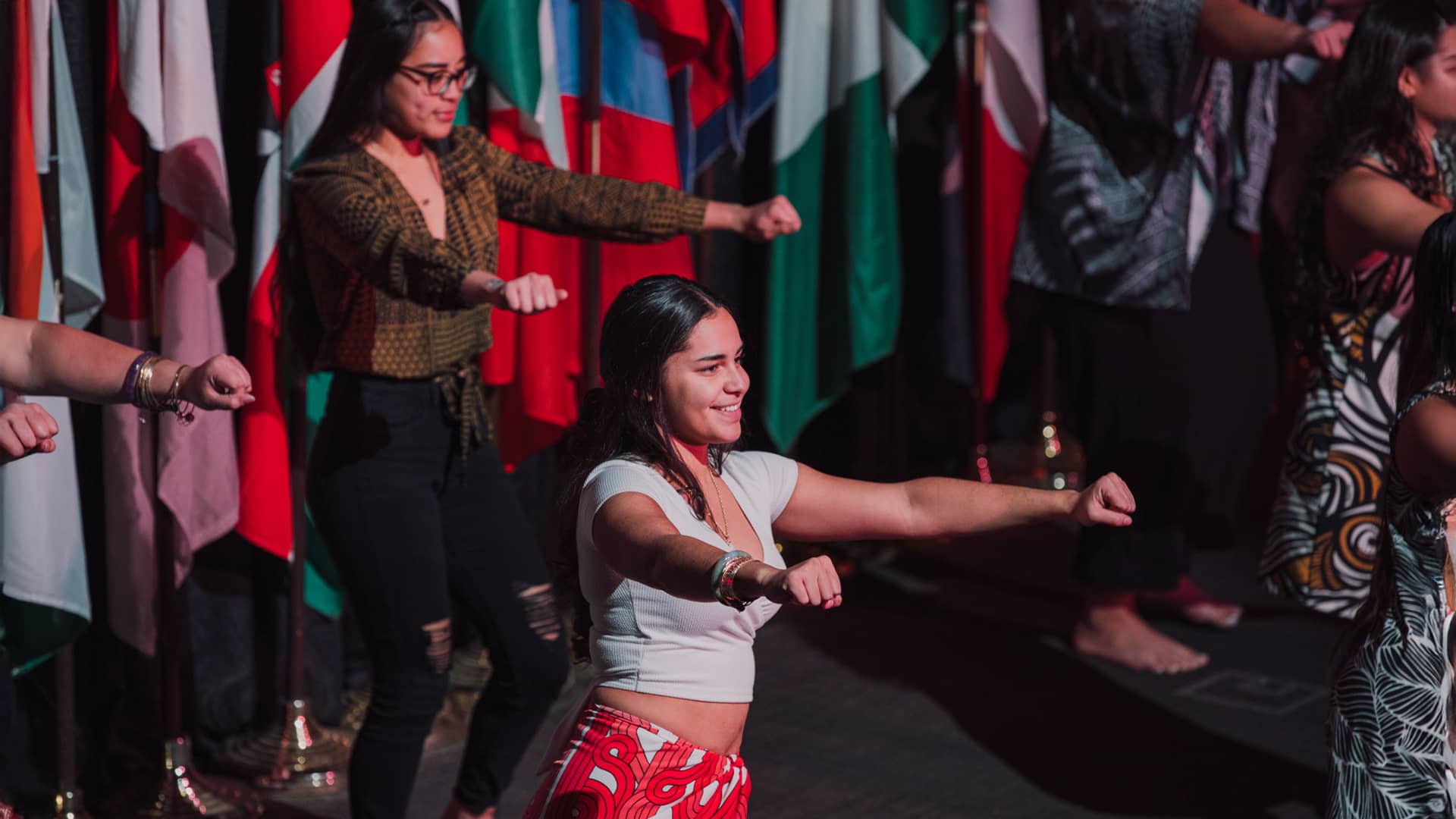 Students dance on a stage with multi-cultural flags and decor.