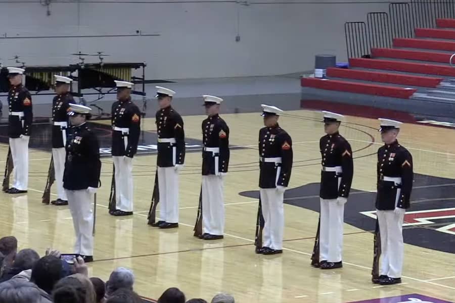 Several marines form a line, standing at attention in a gymnasium.