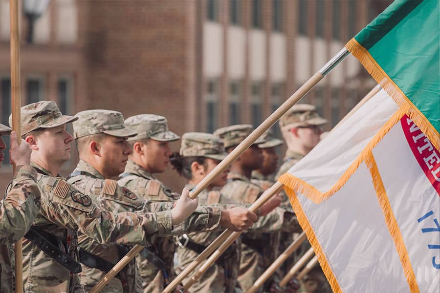 Several military students form a line, bearing flags.