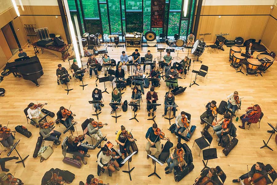 An arial view of a fully symphony rehearsal in a large room with many windows.