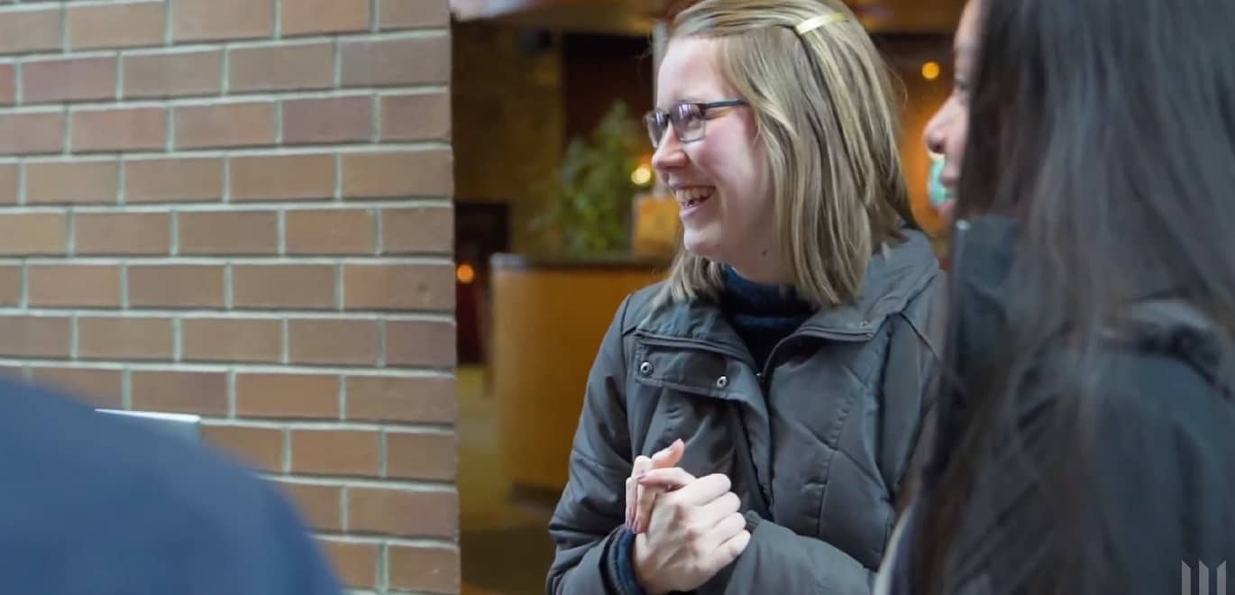 Two students smile and laugh while listening to a speaker not on screen.