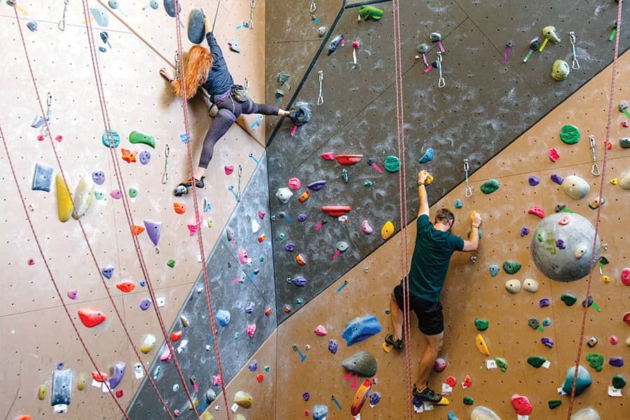 Two students climb a vast climbing wall.