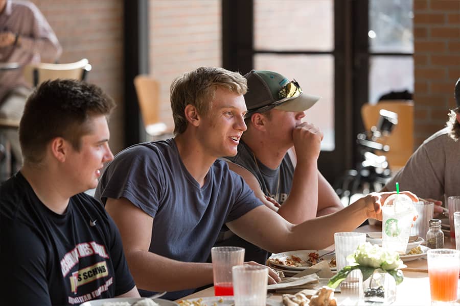 Three students converse over lunch in a sunny cafeteria.