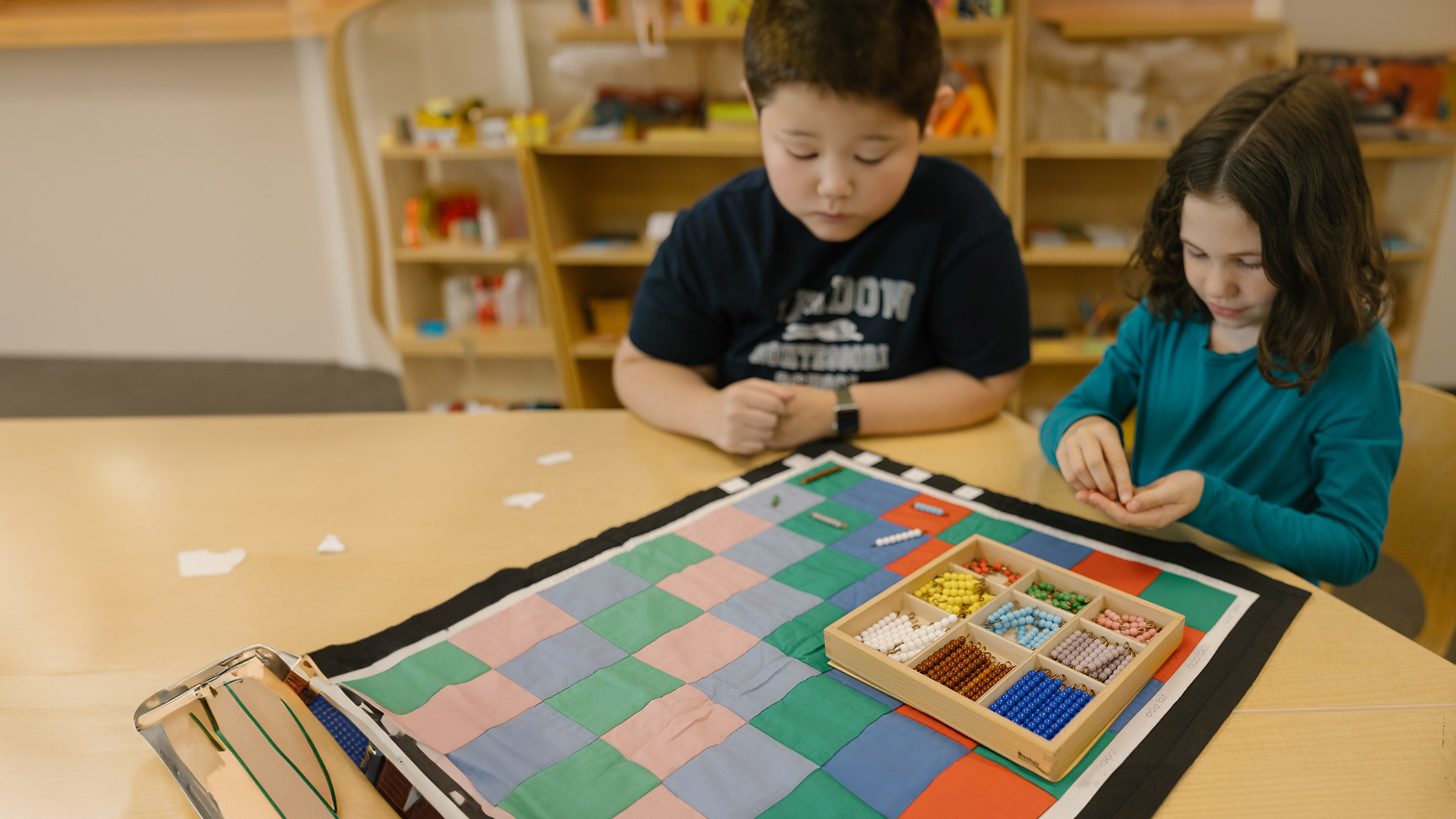 Two children play with beads on a colorful mat in a classroom setting.