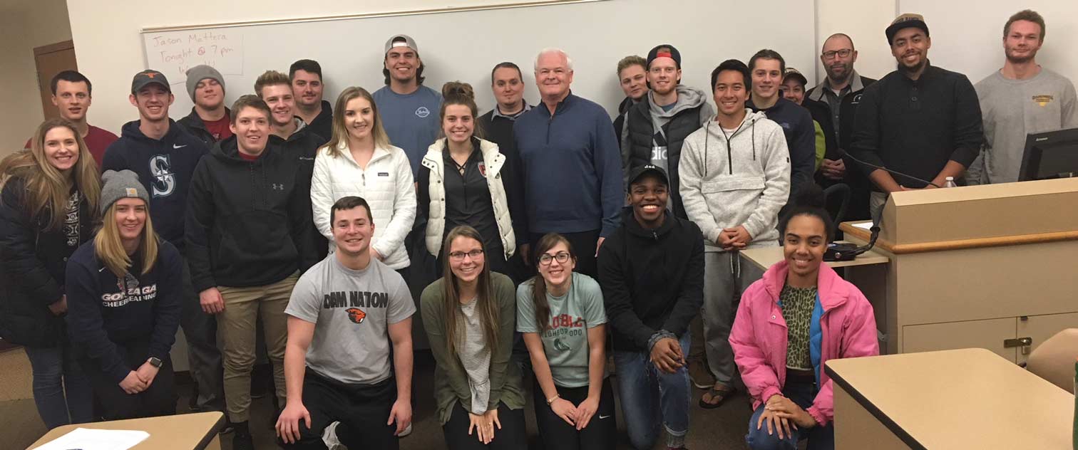 Dan Mahoney and students pose, smiling, in front of a whiteboard in a classroom setting.