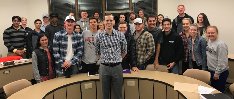 Jay Stahlman poses with a group of students around a semicircle desk.