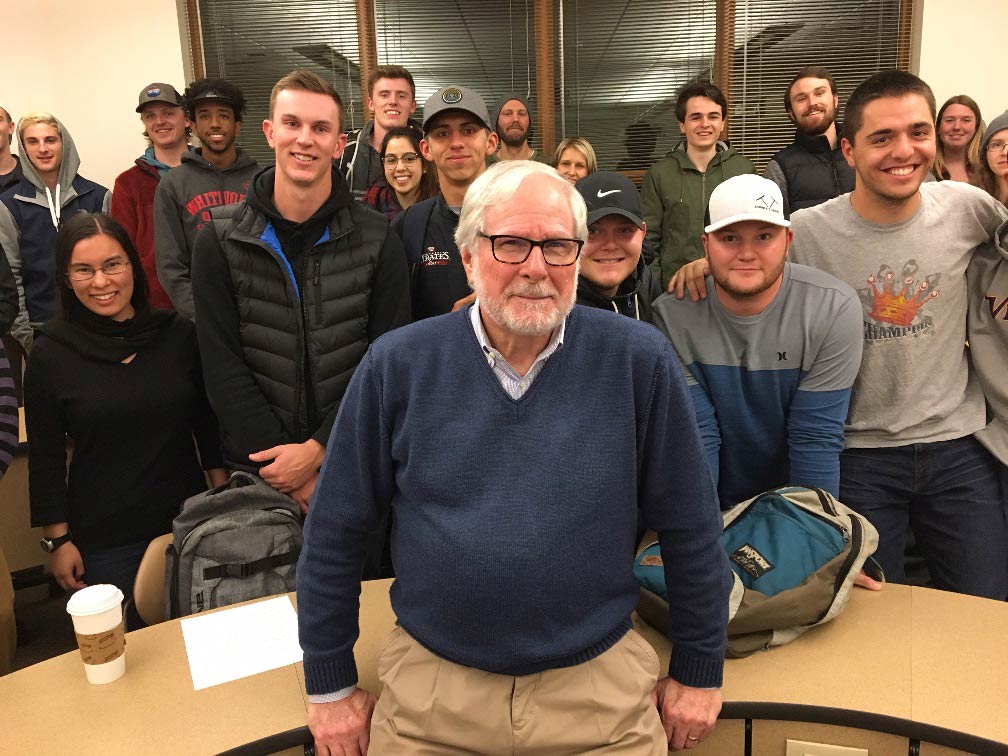 Bill Simmons poses with a group of students around a semicircle desk.