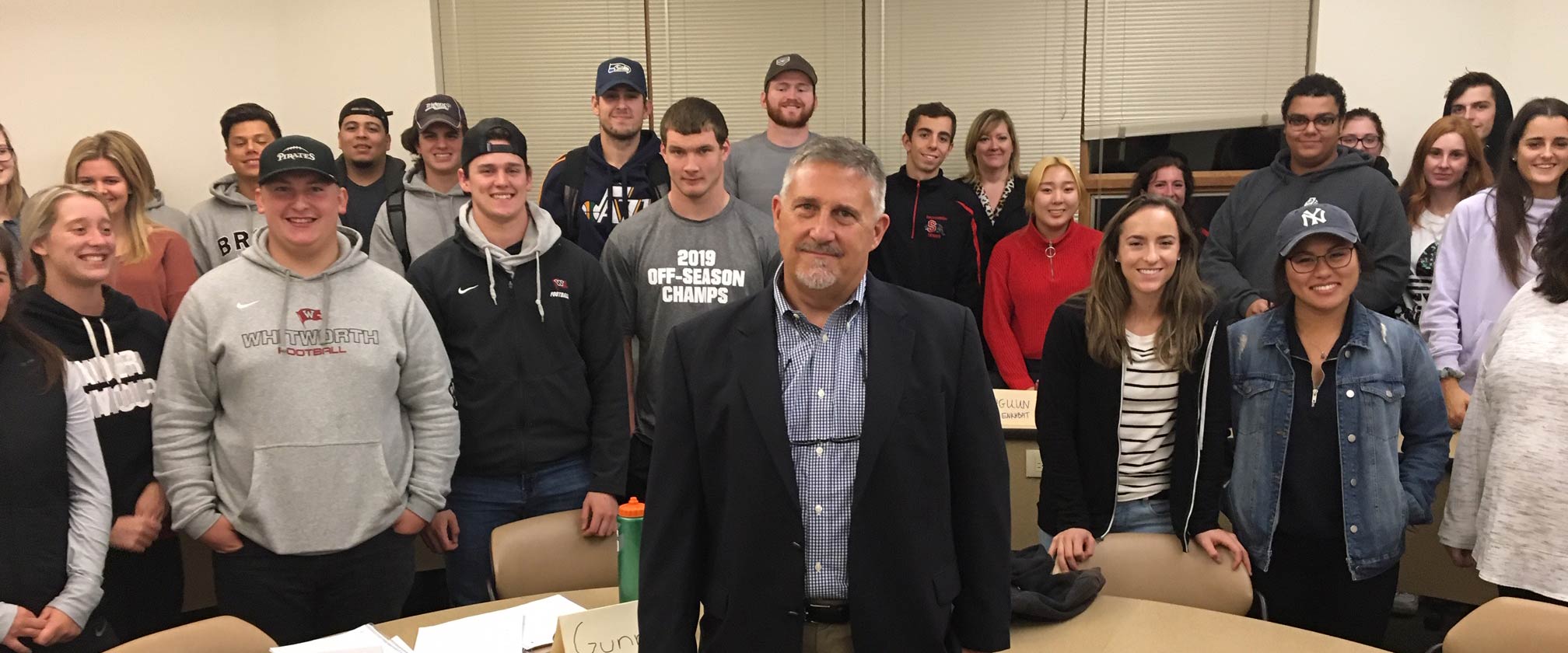 Steve John and students pose, smiling, around a semicircle desk.
