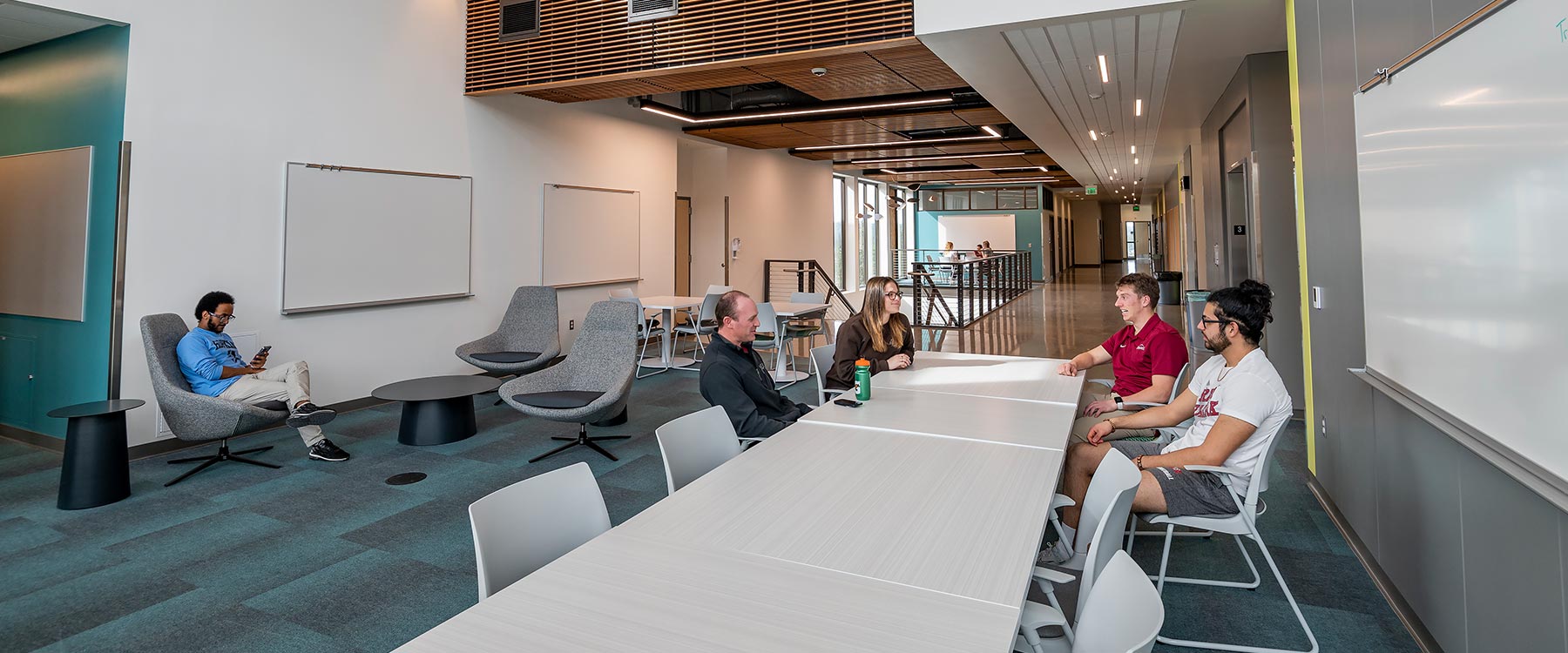 Four people sit and converse at a long table within a spacious, modern co-working space.