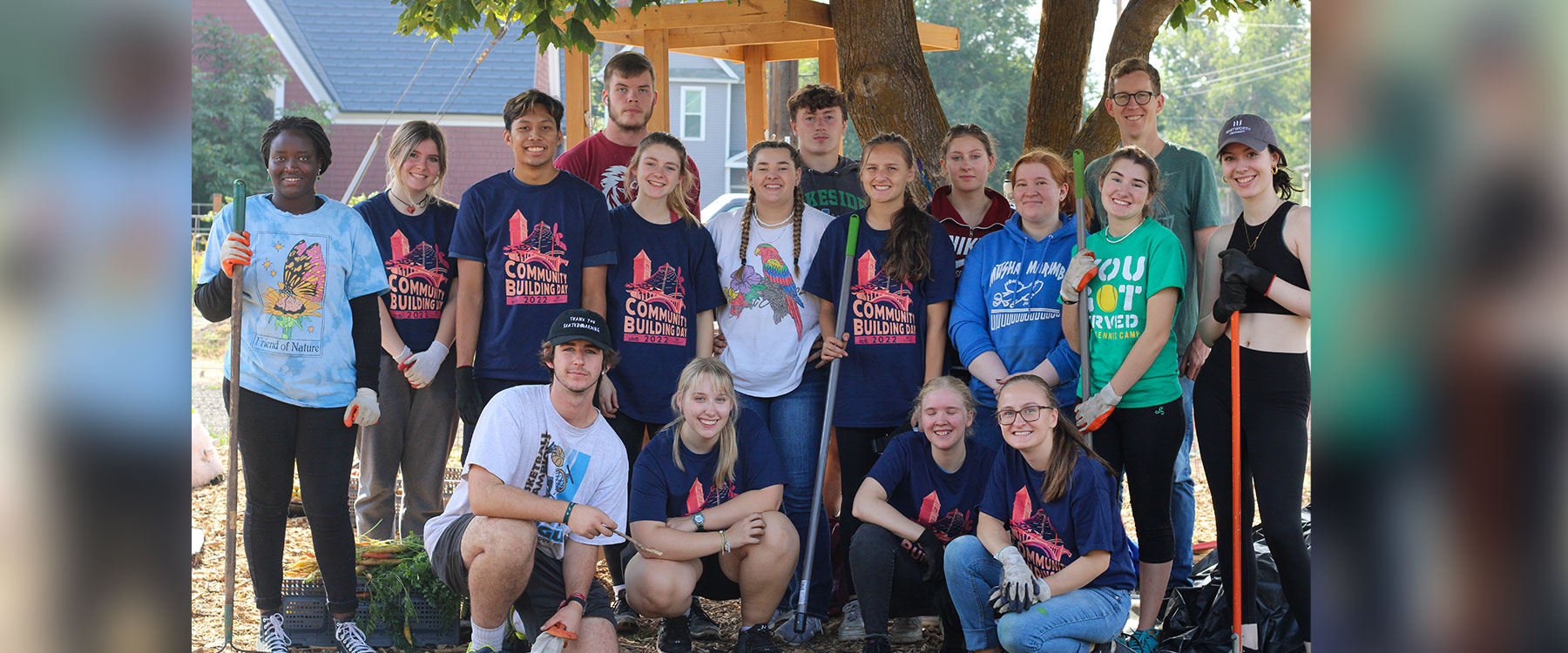 A group of young people gathered outdoors, smiling for a photo, wearing casual clothing and gardening gloves.