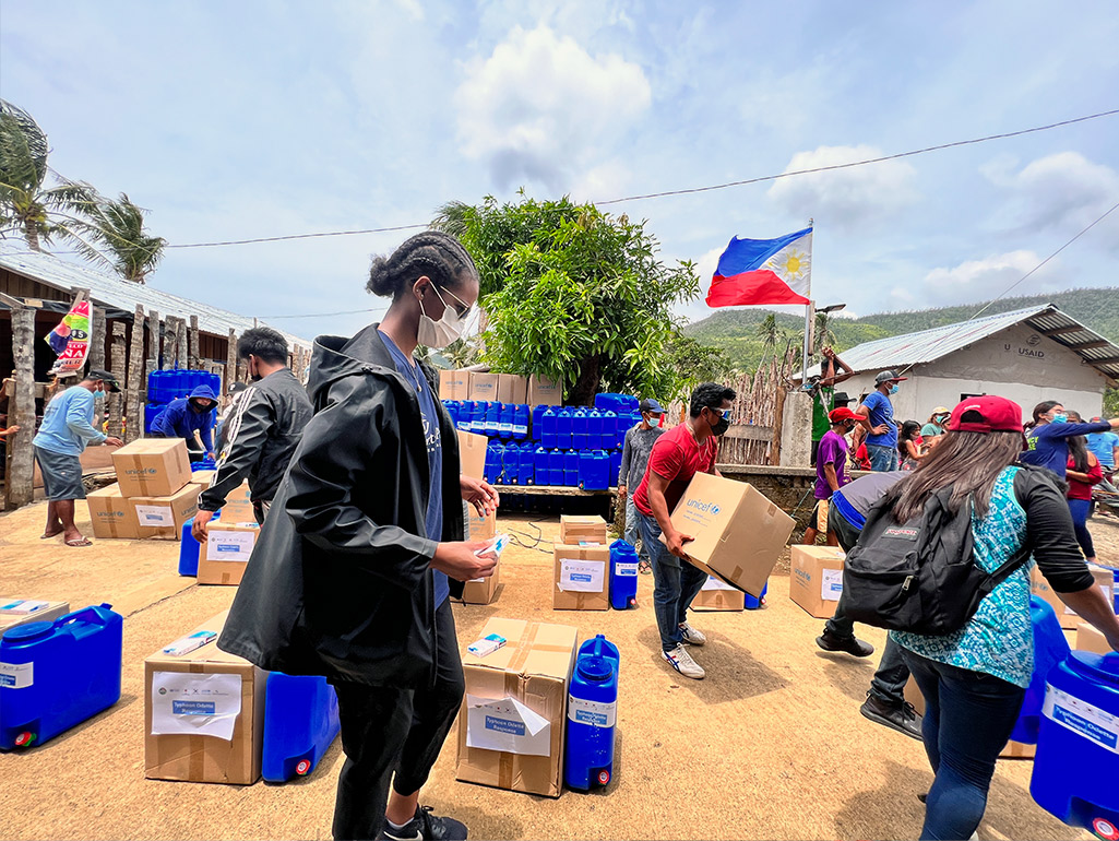 Several people wearing masks organize and distribute aid supplies in a sunny location.
