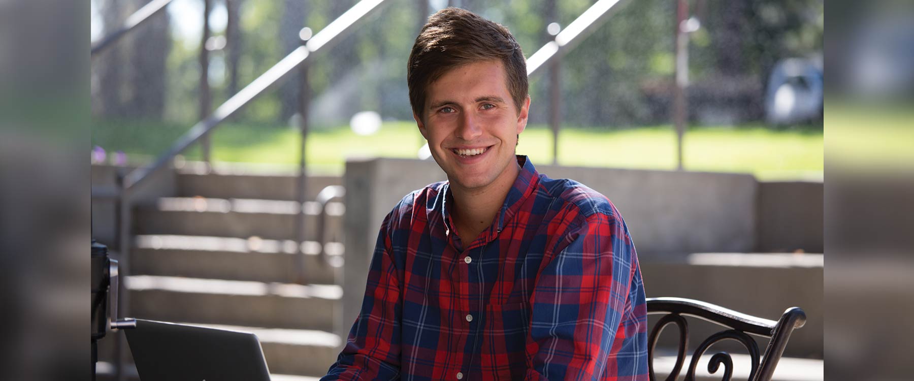Micah sits at a table on the patio outside Cowles Memorial Library and smiles at the camera.