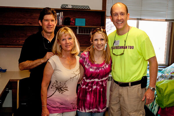 Beck Taylor poses with a student and her parents inside of a Ballard Hall dorm room.