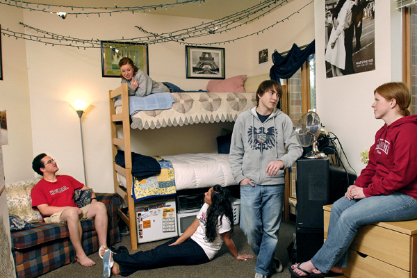 A group of students hang out in a Duvall Hall dorm room with bunk beds, a sofa and twinkle lights.