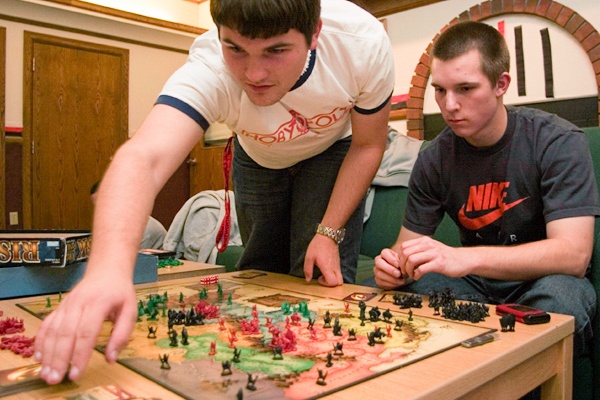 Two students play a strategy board game, one reaching over to move a piece on the game board.