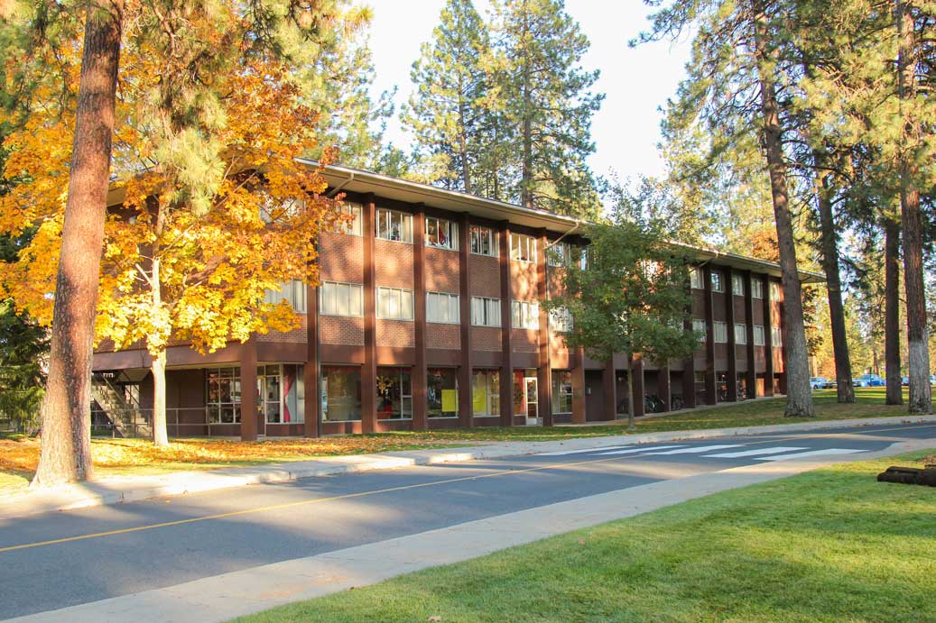 A large, rectangular three-story residence hall surrounded by autumn trees on a clear day.